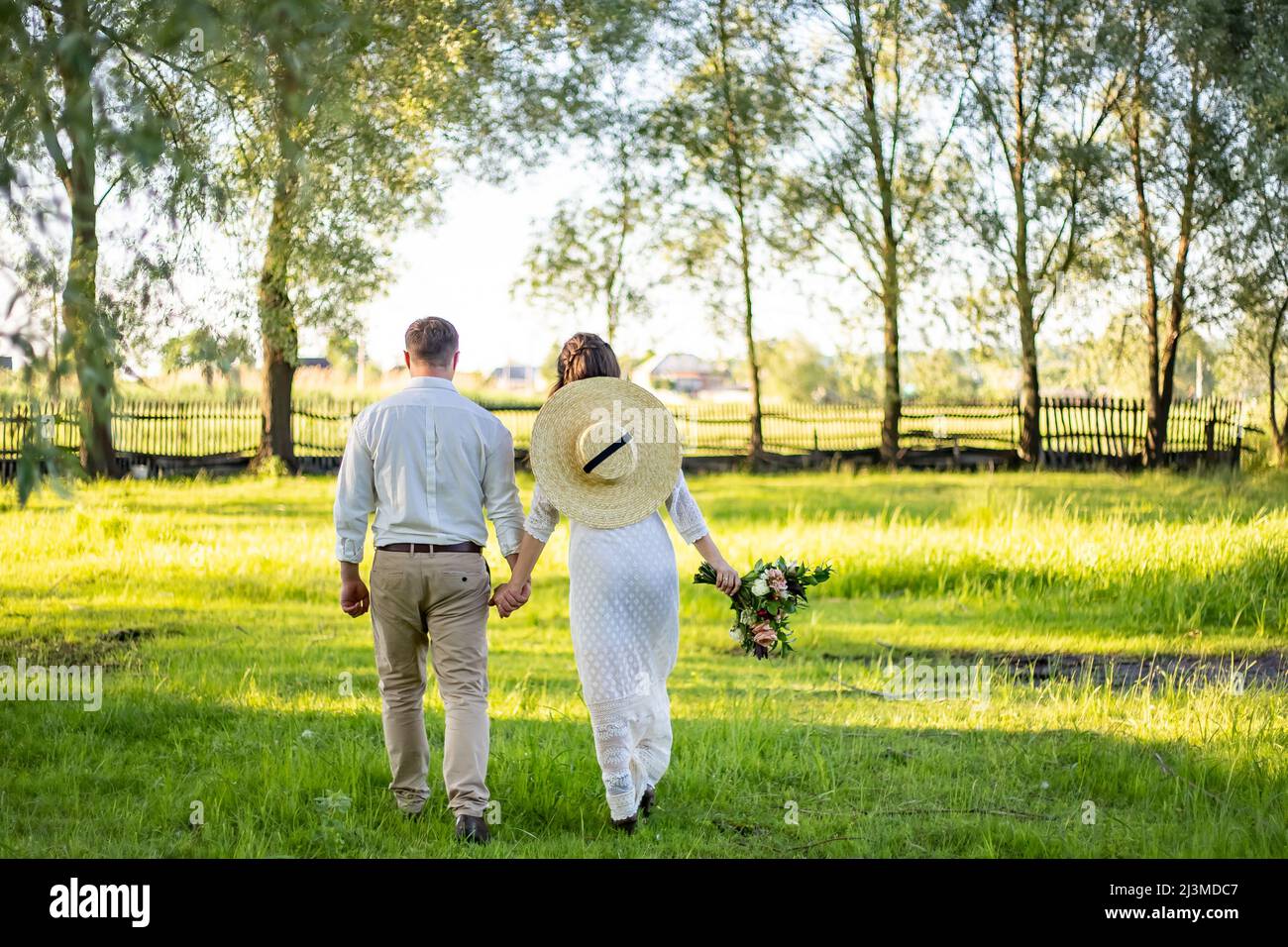 Le couple traverse le champ. Ils ont hans. Le voile se dissipe. Dans les mains d'un bouquet Banque D'Images