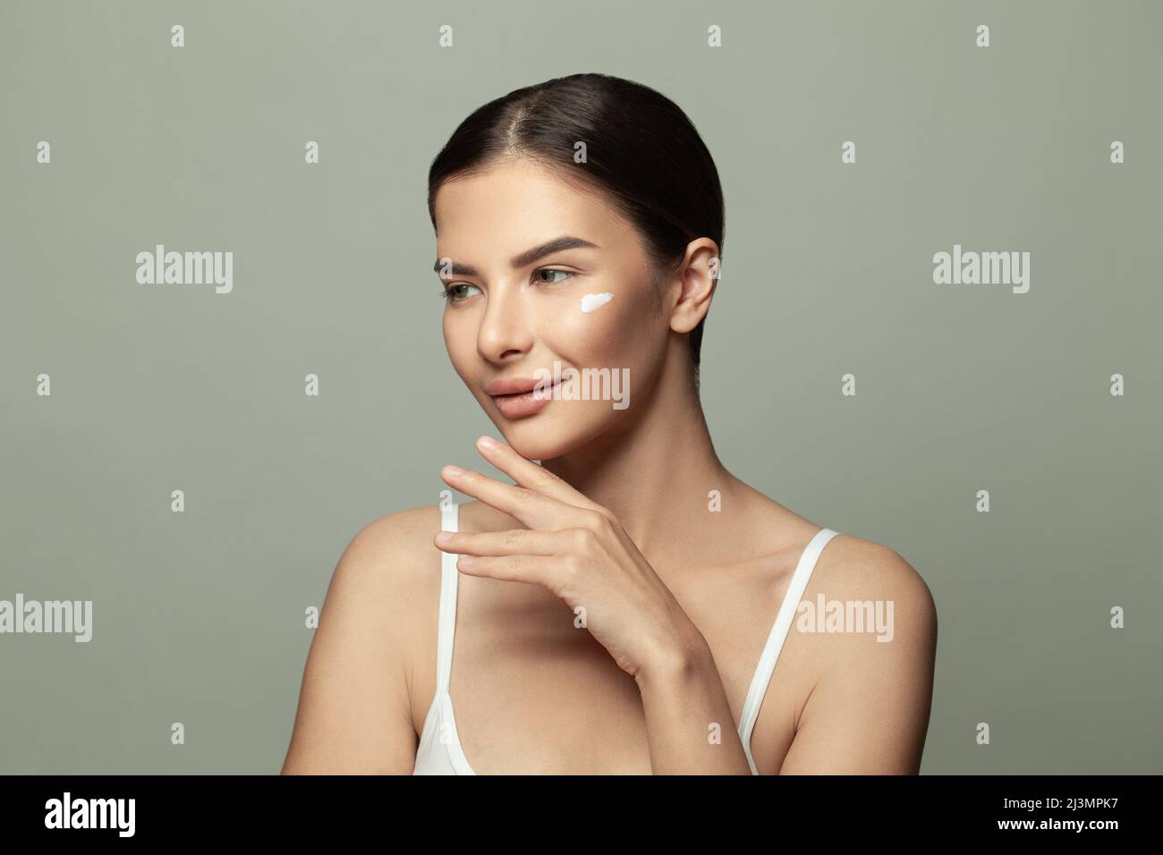 Portrait d'une jeune femme appliquant de la crème hydratante sur son joli visage. Concept spa, beauté et soins de la peau Banque D'Images