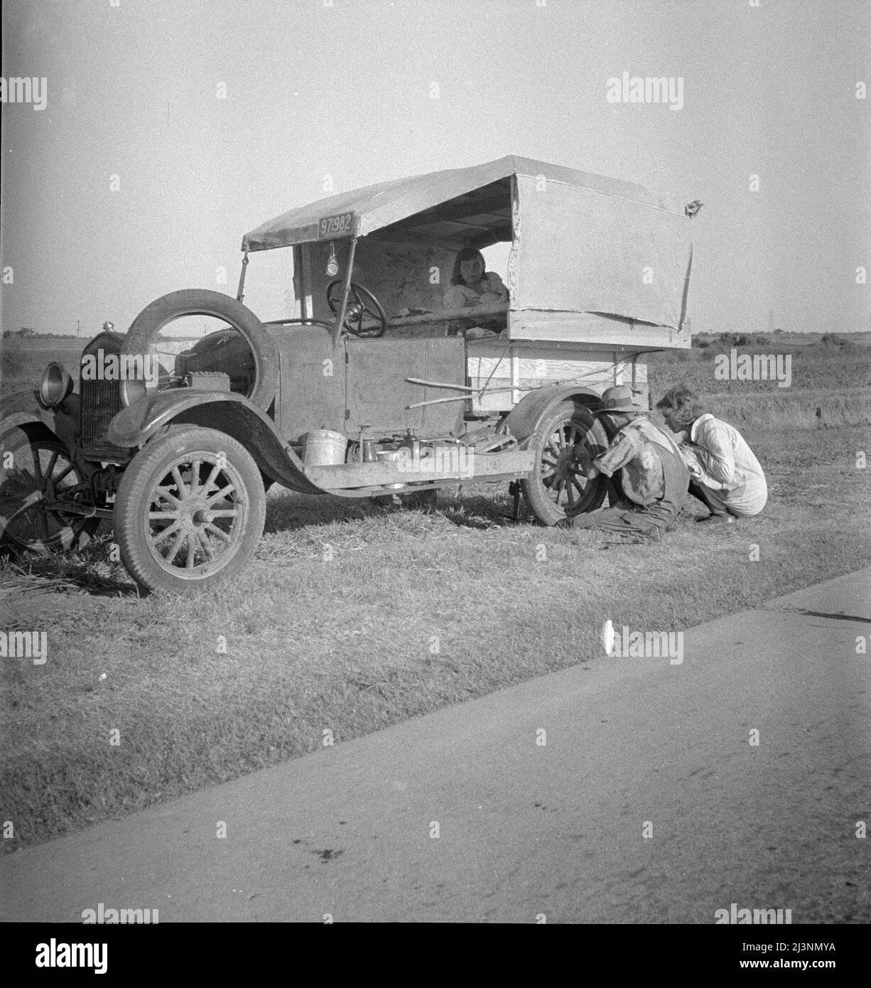 Famille entre Dallas et Austin, Texas. Les gens ont quitté leur maison et leurs connexions dans le sud du Texas, et espèrent atteindre le delta de l'Arkansas pour le travail dans les champs de coton. Personnes sans pénitence. Pas de nourriture et trois gallons de gaz dans le réservoir. Le père tente de réparer un pneu. Trois enfants. Le père dit, "c'est dur, mais la vie est dure de toute façon que vous le prenez". Banque D'Images