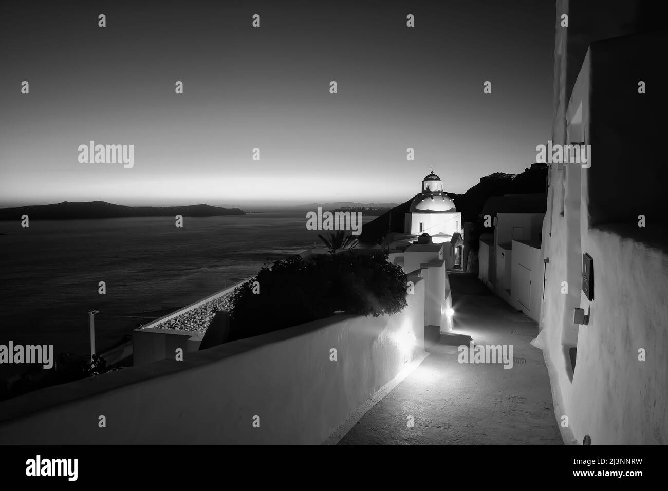 Une allée illuminée menant à une église de Fira Santorini et un coucher de soleil coloré en noir et blanc Banque D'Images