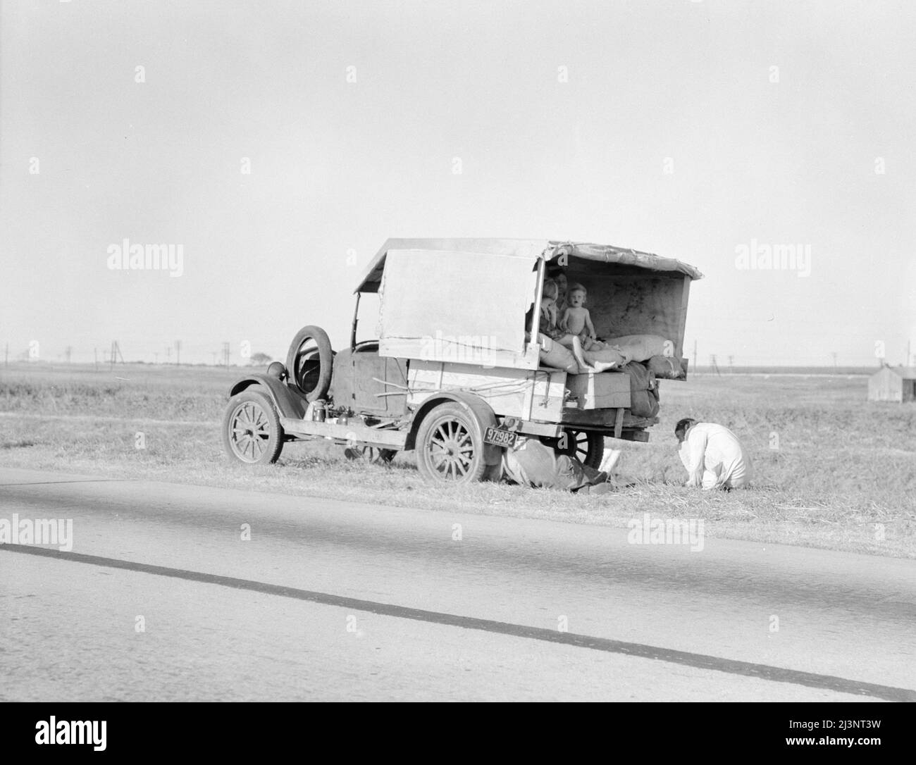 Famille entre Dallas et Austin, Texas. Les gens ont quitté leur maison et leurs connexions dans le sud du Texas, et espèrent atteindre le delta de l'Arkansas pour le travail dans les champs de coton. Personnes sans pénitence. Pas de nourriture et trois gallons de gaz dans le réservoir. Le père essaie de réparer un pneu. Trois enfants. Le père dit, "c'est dur mais la vie est dure de toute façon que vous le prenez". Banque D'Images