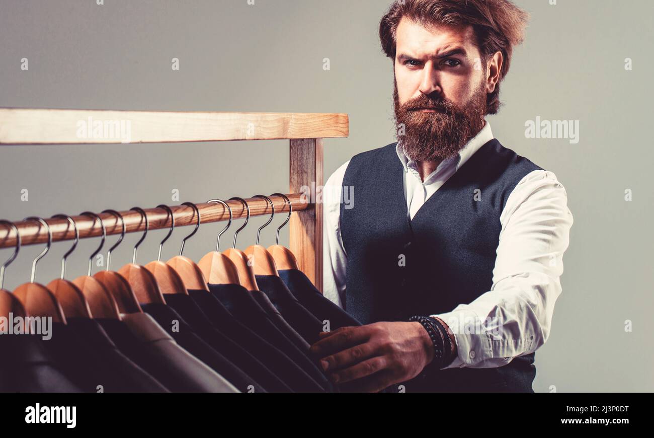 Costume d'homme, tailleur dans son atelier. Costumes de sexe masculin accrochés à la suite. Sur mesure. Costume élégant pour homme. Beau homme de mode barbu classique Banque D'Images