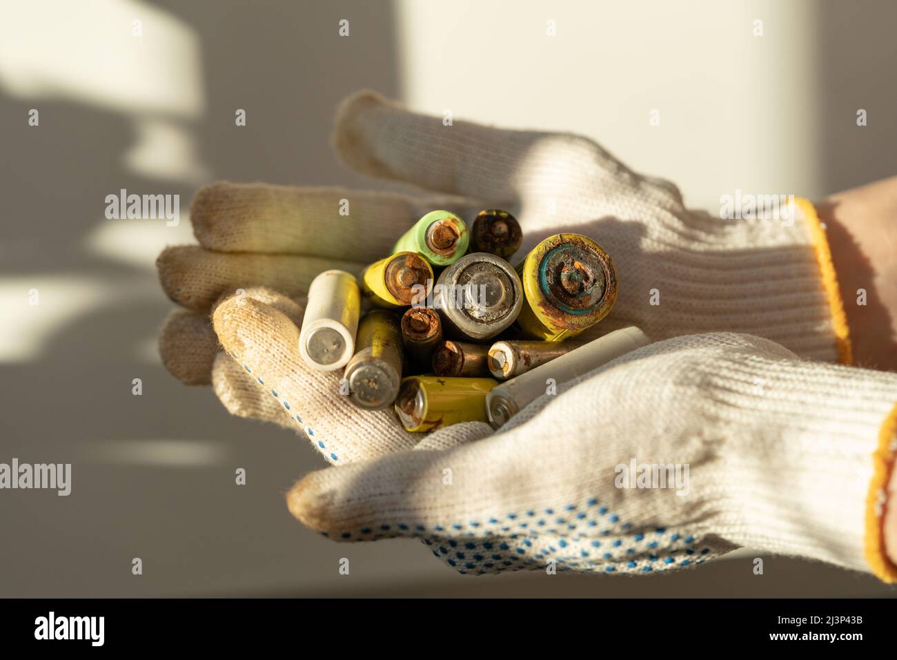 Gros plan des mains des femmes dans des gants de protection en coton tenant le tas de piles alcalines usagées Banque D'Images