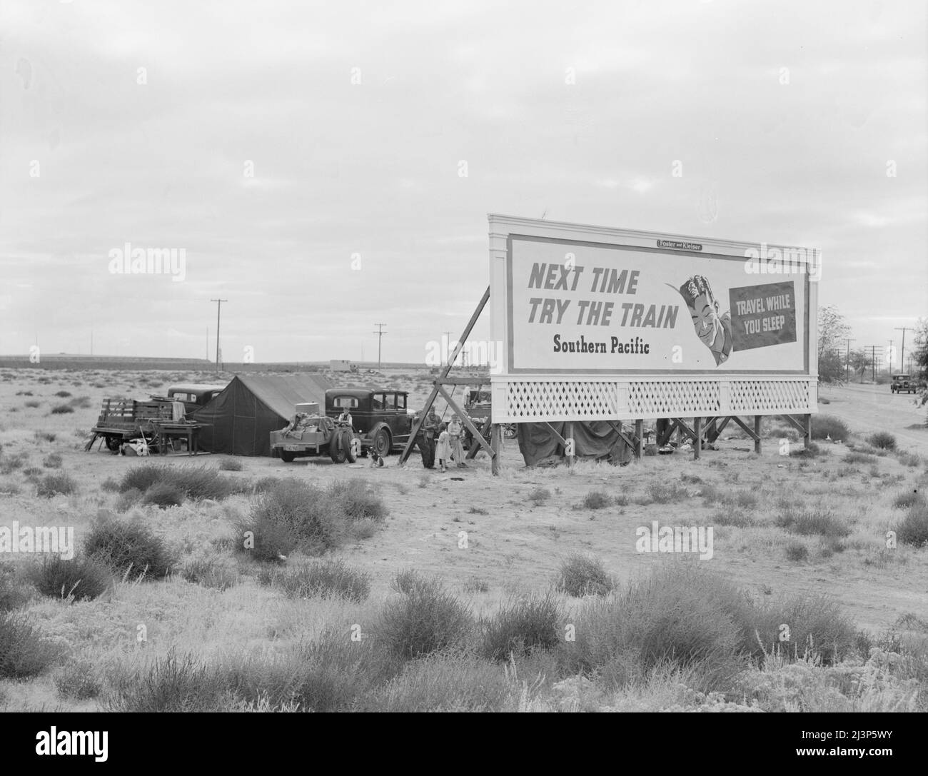Panneaux le long des États-Unis 99 derrière lesquels trois familles de migrants indigents sont campés. Kern County, Californie. [Annonce: 'Prochaine fois essayez le train - Voyage pendant que vous dormez - Pacifique Sud']. Banque D'Images