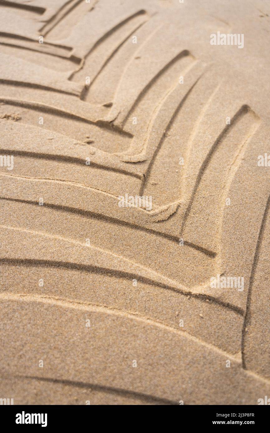 Les empreintes de pneus de tracteur sont incrustées dans une plage de sable avec un motif géométrique. Les chenilles des pneus de véhicules sont en gros plan avec une texture sablonneuse au bord de la mer. Banque D'Images