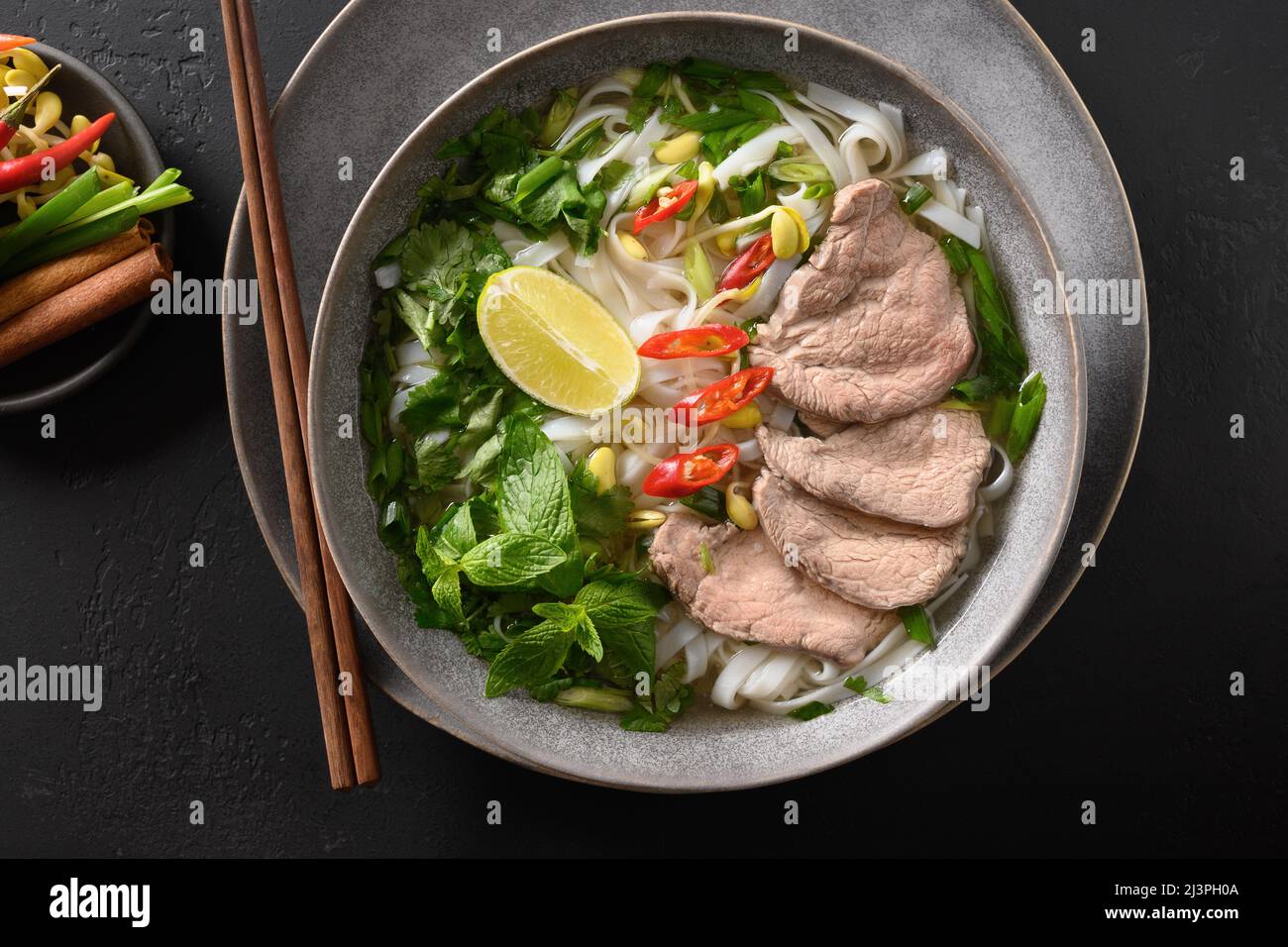 Soupe traditionnelle Pho Bo avec bœuf, nouilles de riz, gingembre, lime, piment dans un bol sur fond noir.Vue de dessus.Cuisine vietnamienne et asiatique Banque D'Images