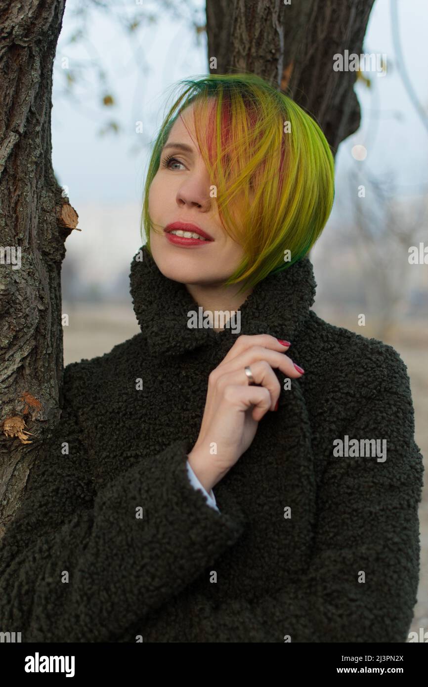 Femme seule avec ses pensées seule avec des cheveux multicolores près d'un arbre. Banque D'Images