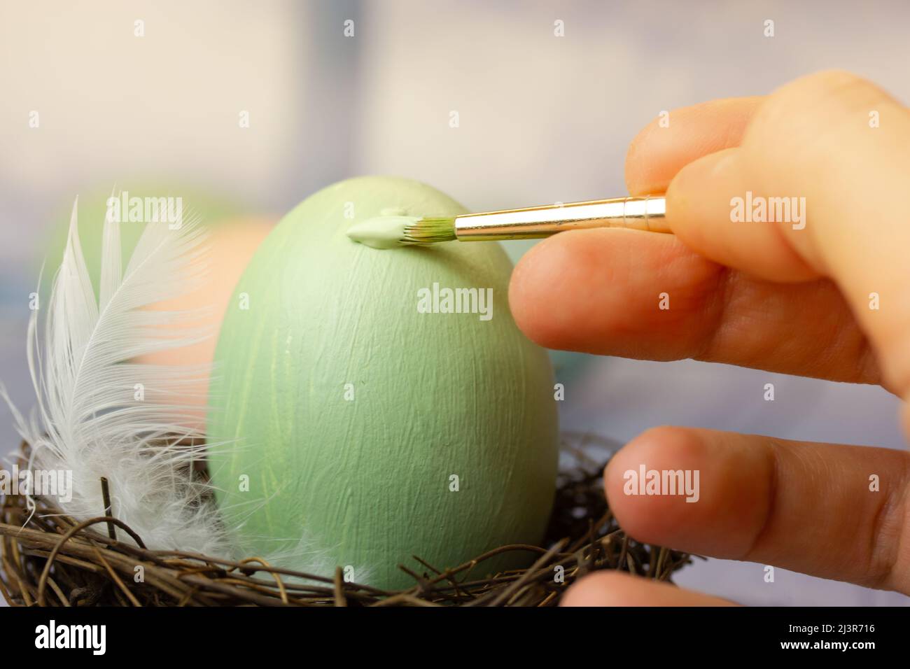 Procédé de peinture d'un oeuf de Pâques dans un nid avec une peinture de couleur pastel vert clair. Un pinceau dans la main d'une femme. Préparation pour des vacances de printemps Banque D'Images