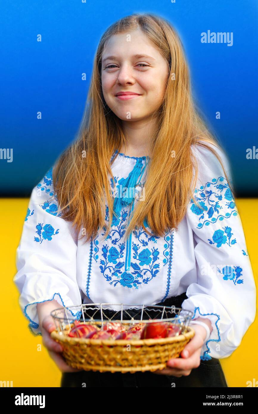 Recentrer la jeune fille ukrainienne dans vyshyvanka tenant le panier d'oeufs rouges colorés sur fond de drapeau ukrainien. Pâques, Ukraine. Œufs peints artisanaux. Collection Banque D'Images