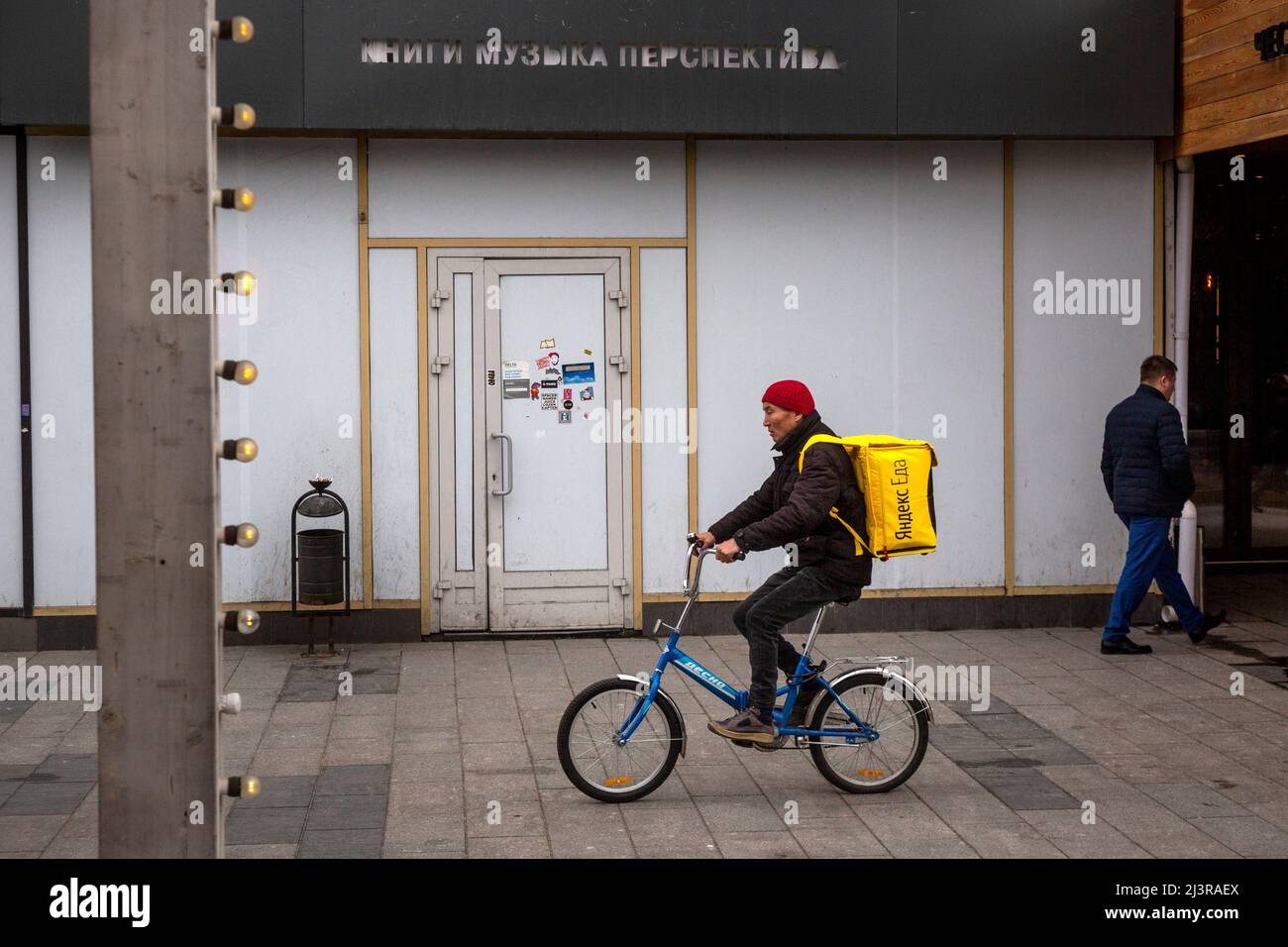 Moscou, Russie. 9th avril 2022. Un messager du service de livraison Yandex EDA se trouve à vélo le long de la rue Novy Arbat, sur fond d'une librairie fermée Respublika (Eng: Republic) à Moscou, en Russie. L'inscription au-dessus de l'entrée fermée indique « Book Music perspective » Banque D'Images