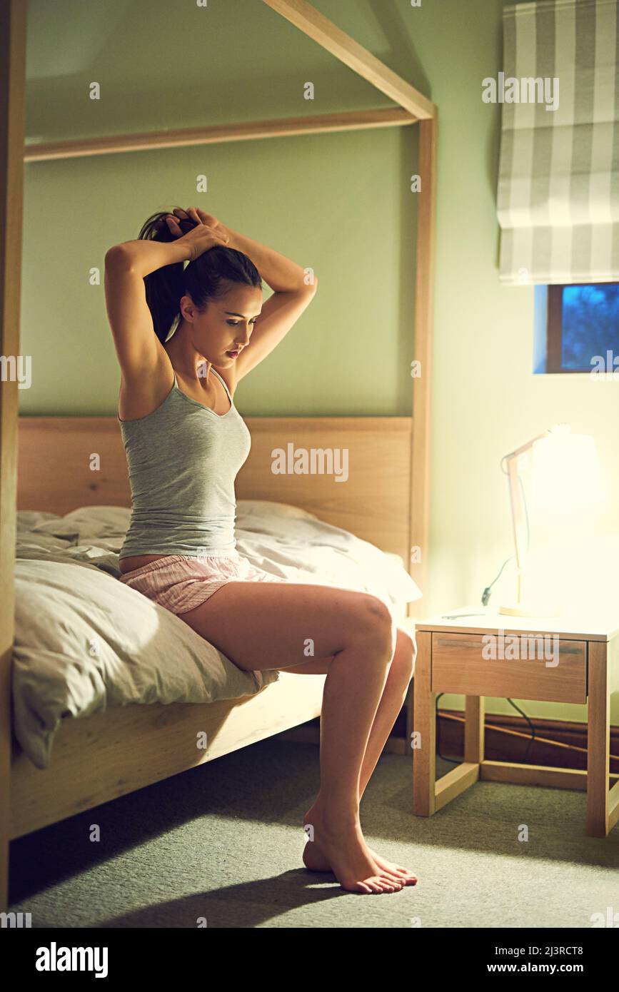 Il est temps de dormir. Prise de vue d'une jeune femme qui noue ses cheveux en arrière tout en se prépare à se coucher dans sa chambre. Banque D'Images