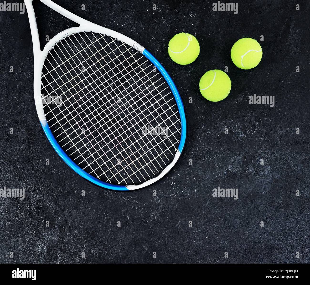 C'est à votre tour de servir. Photo en grand angle d'une seule raquette de tennis et de quelques balles de tennis placées sur un fond sombre à l'intérieur d'un studio. Banque D'Images