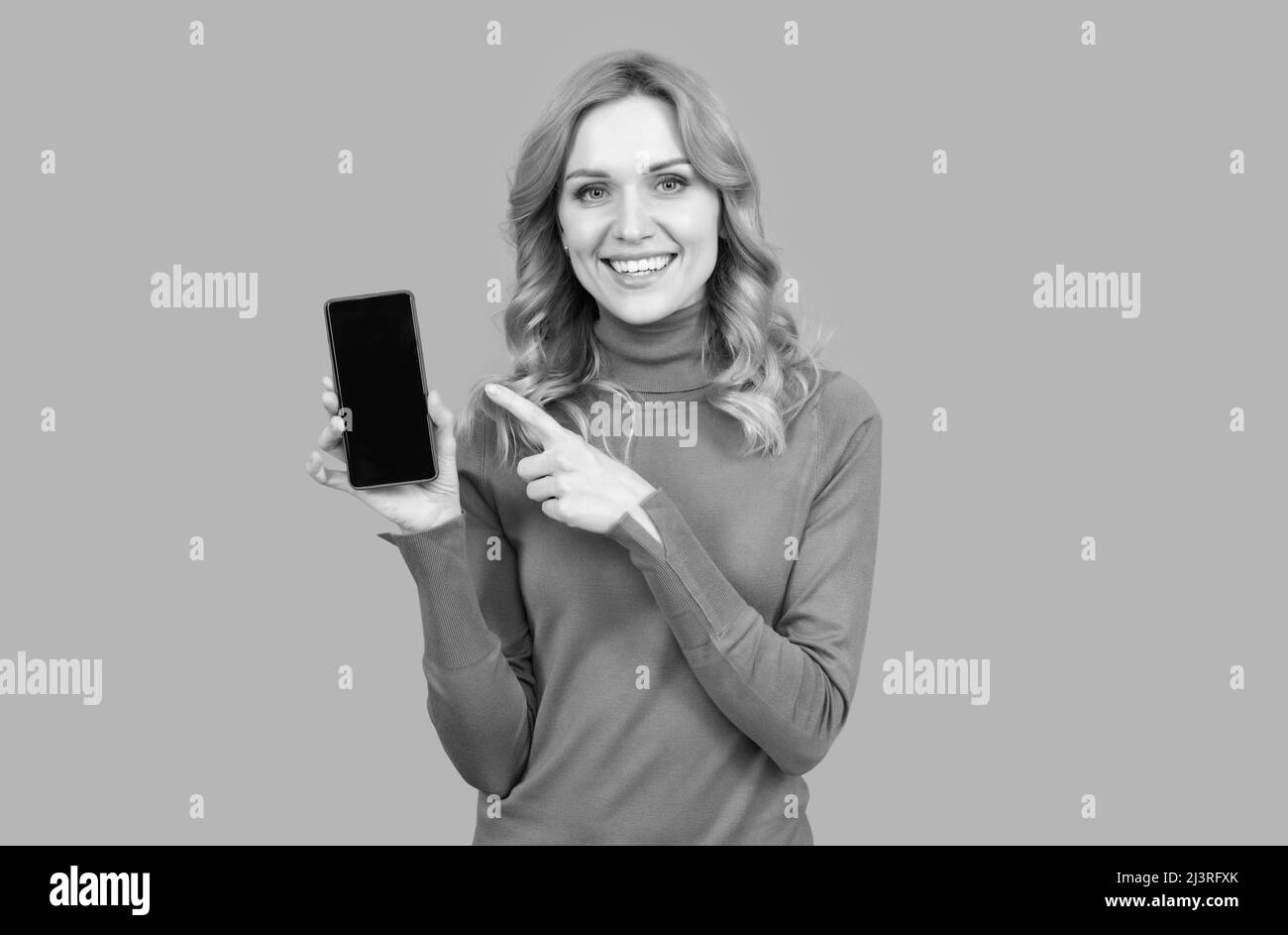 Une femme pointe le doigt sur l'écran vide de téléphone portable fond gris espace de copie, publicité smartphone. Banque D'Images
