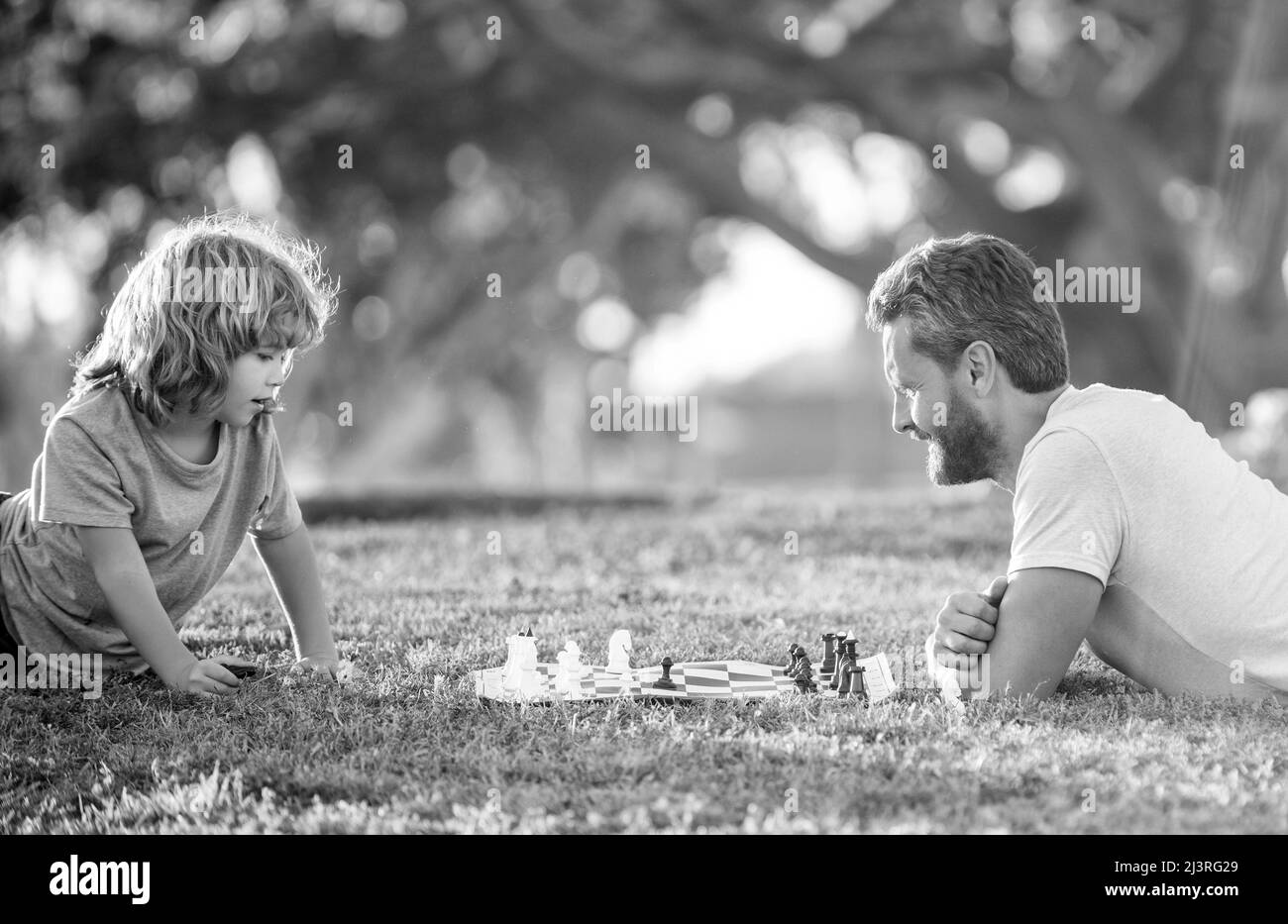 bonne famille de papa et son enfant jouant aux échecs sur l'herbe verte dans le parc extérieur, jeu de société Banque D'Images