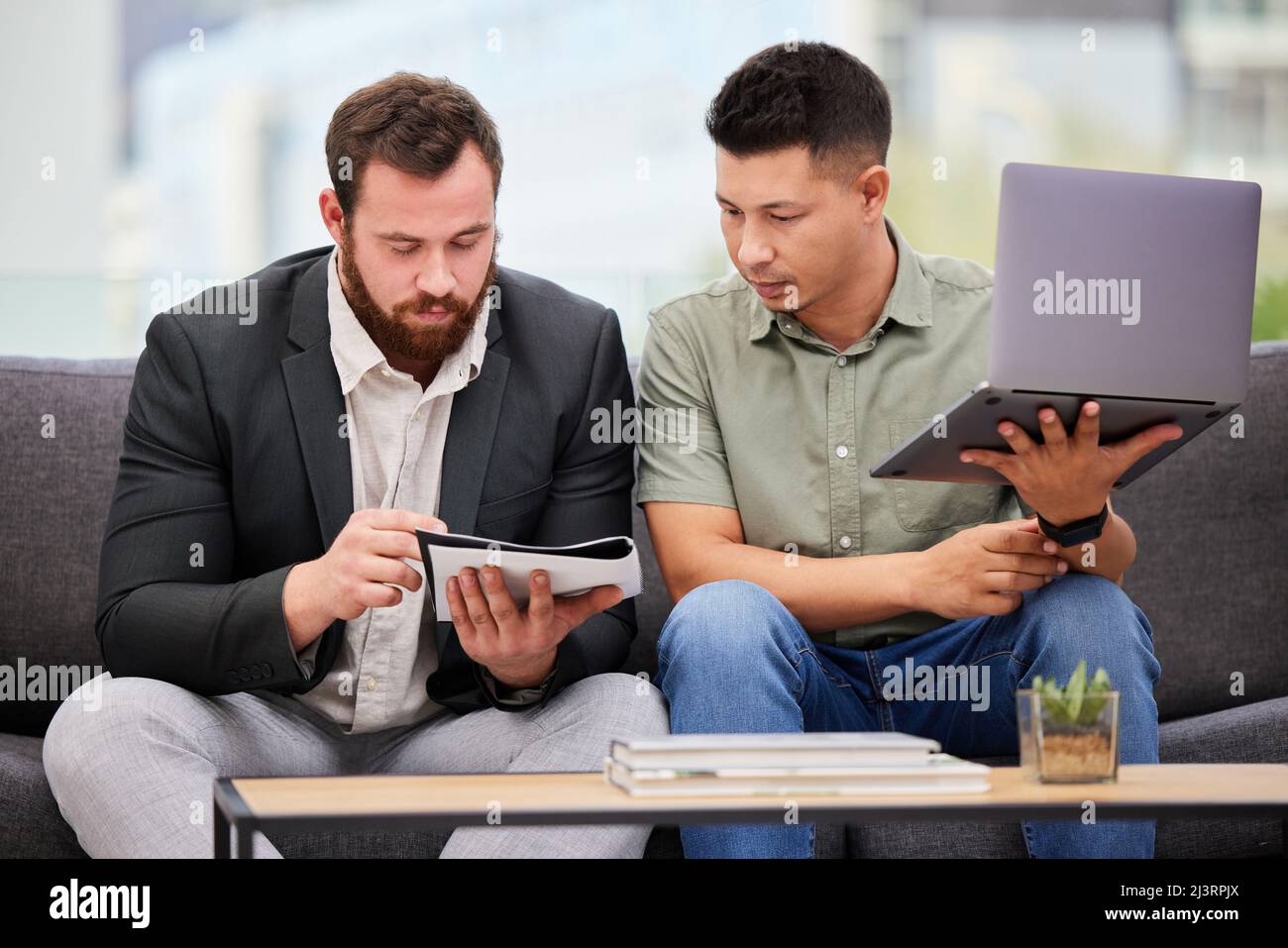Formuler des plans novateurs. Photo de deux hommes d'affaires qui passent par la paperasse tout en utilisant un ordinateur portable ensemble dans un bureau. Banque D'Images