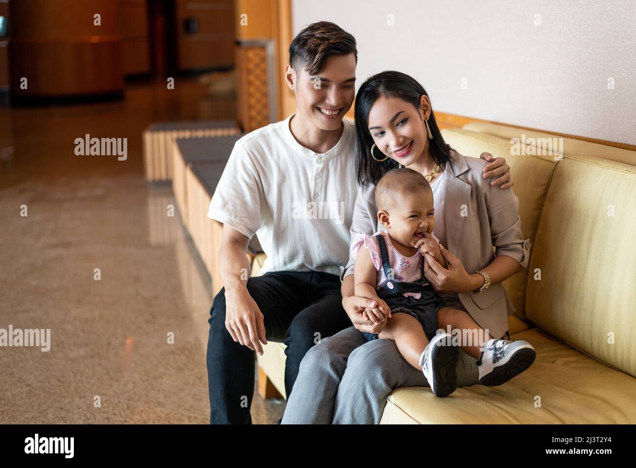 Malay asiatique malaisien Jeune couple musulman avec une fille d'un an assise sur un long canapé-chaise marron clair, cheveux longs, pleine longueur ou à la taille Banque D'Images