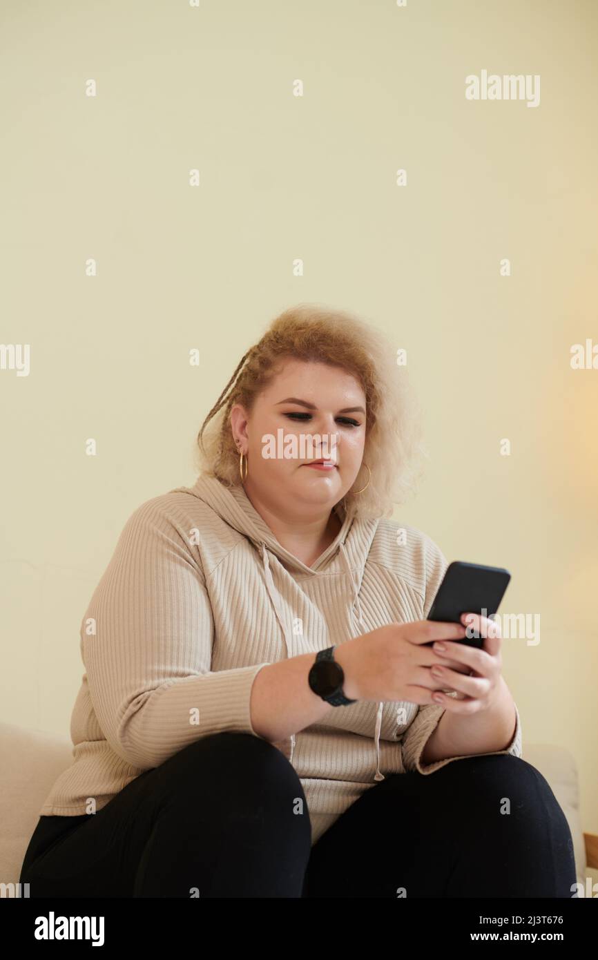 Une jeune femme de plus grande taille lit des messages texte de ses amis sur son smartphone Banque D'Images