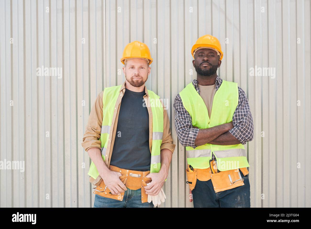 Les constructeurs de gilets de sécurité et de casques de sécurité sont assis sur une poutre de ciment et parlent tout en se relaxant sur le chantier de construction pendant la pause-café Banque D'Images