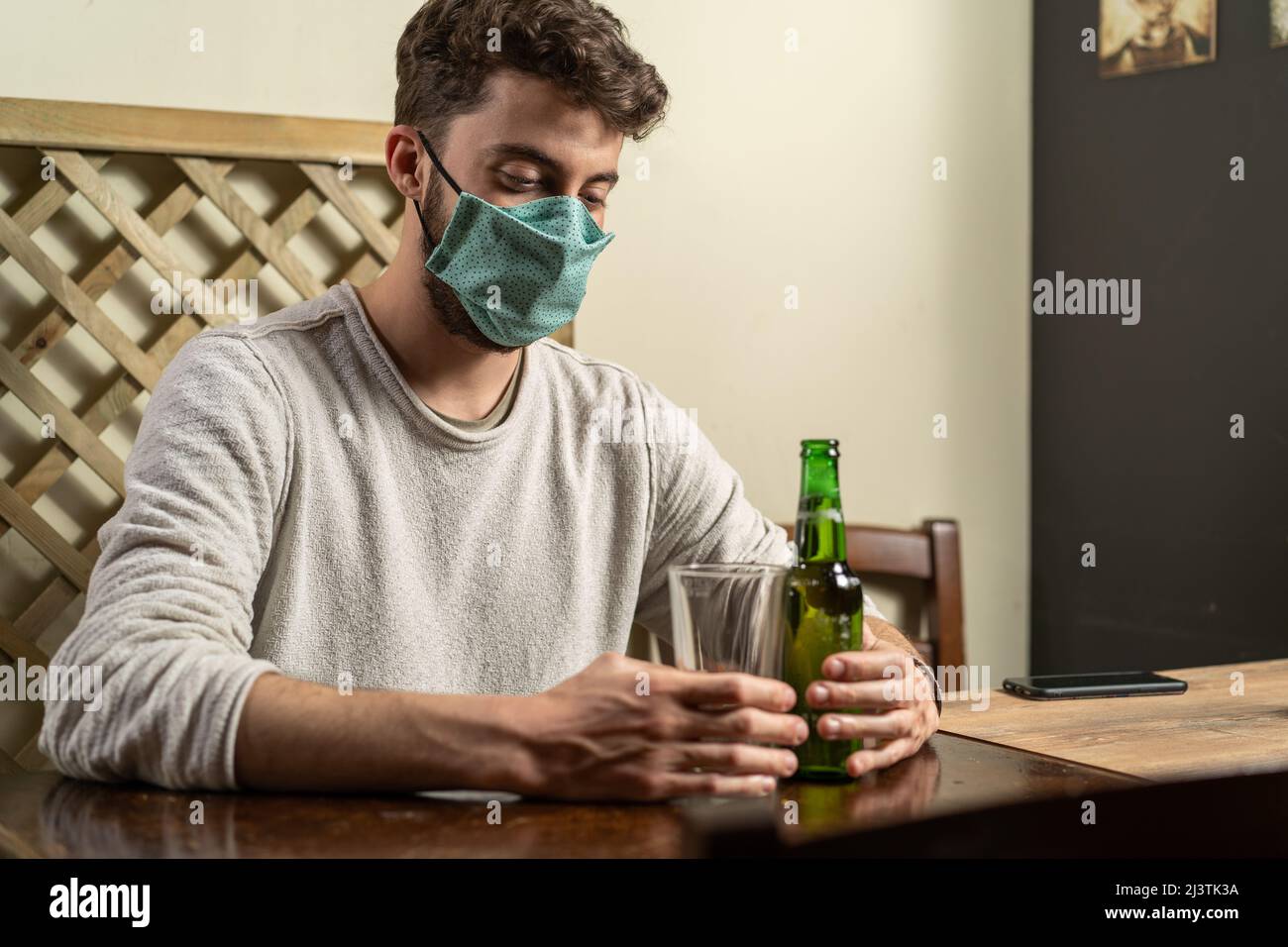 Guy avec masque de mode boire de la bière seule dans un pub intérieur. Nouveau concept normal de jeunes nouveaux comportements pendant le virus corona (Covid-19) pandem Banque D'Images