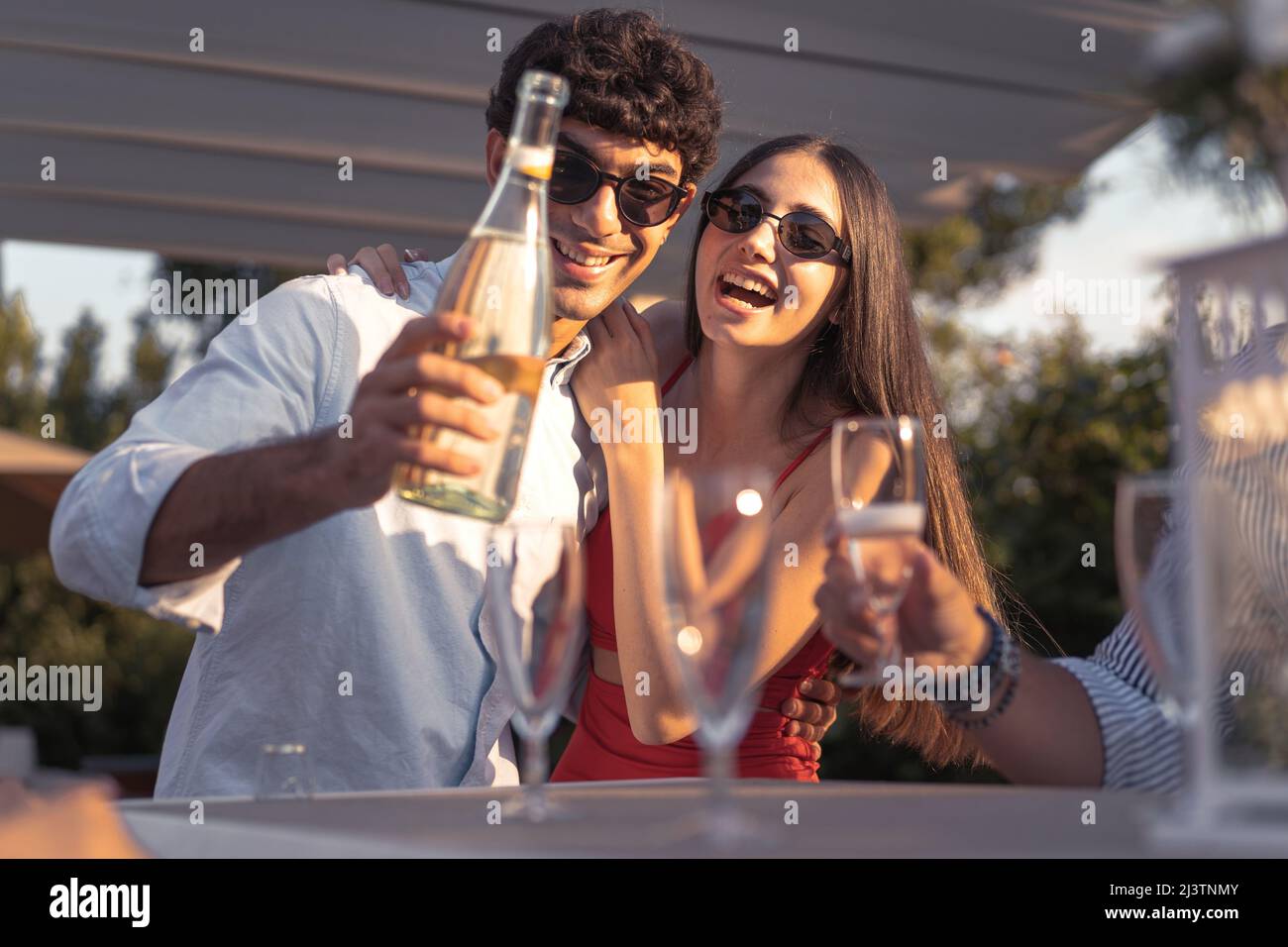 Couple de jeunes engagés qui versent du champagne dans des flûtes célébrant leur amour - amis gaies buvant du vin mousseux souriant et du havi Banque D'Images