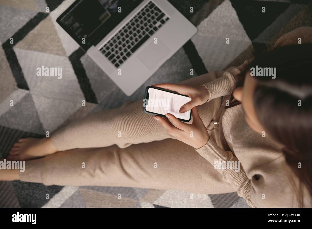 Femme tenant une carte de crédit et utilisant le téléphone assis sur le sol. Paiement. Shopping en ligne vue de dessus Banque D'Images