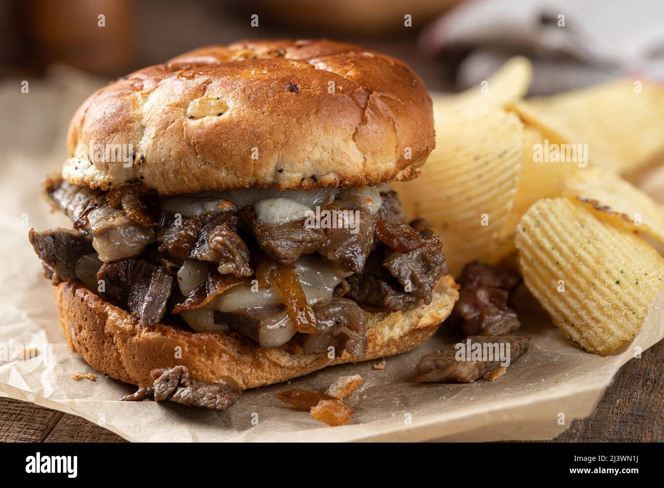 Gros plan d'un sandwich cheesesteak chaud sur un pain grillé avec des chips de pommes de terre sur une table rustique en bois Banque D'Images