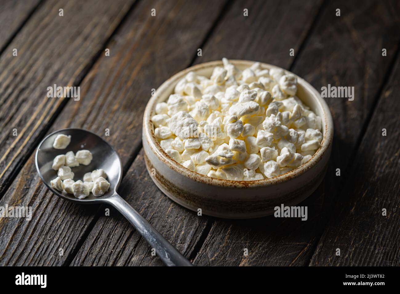 Farmers cottage fromage dans un bol en argile, à côté d'une cuillère sur fond de bois foncé, gros plan. Nourriture saine naturelle, alimentation saine Banque D'Images