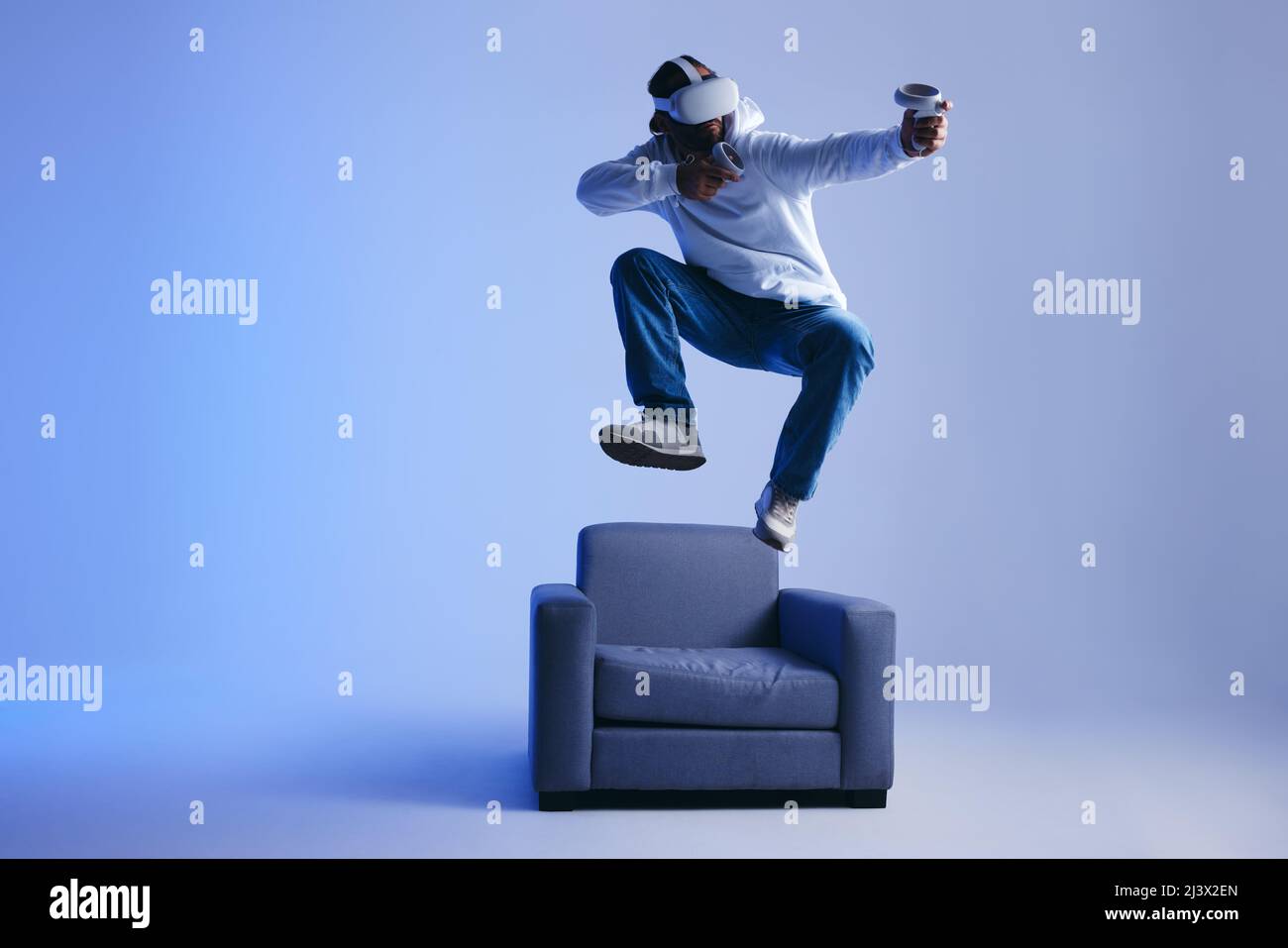 Jeune homme énergique jouant un jeu de réalité virtuelle immersif dans un studio. Homme jouant avec des lunettes de réalité virtuelle et des contrôleurs. Jeune homme ayant f Banque D'Images