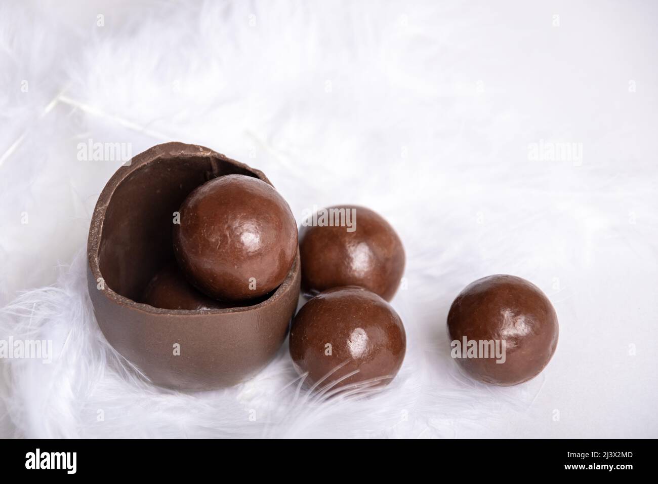 Chocolat fissuré oeuf de pâques avec chocolat petits bonbons ronds dans un nid de plumes blanches, espace de copie. Chocolat pour les enfants. Concept de Pâques. Banque D'Images