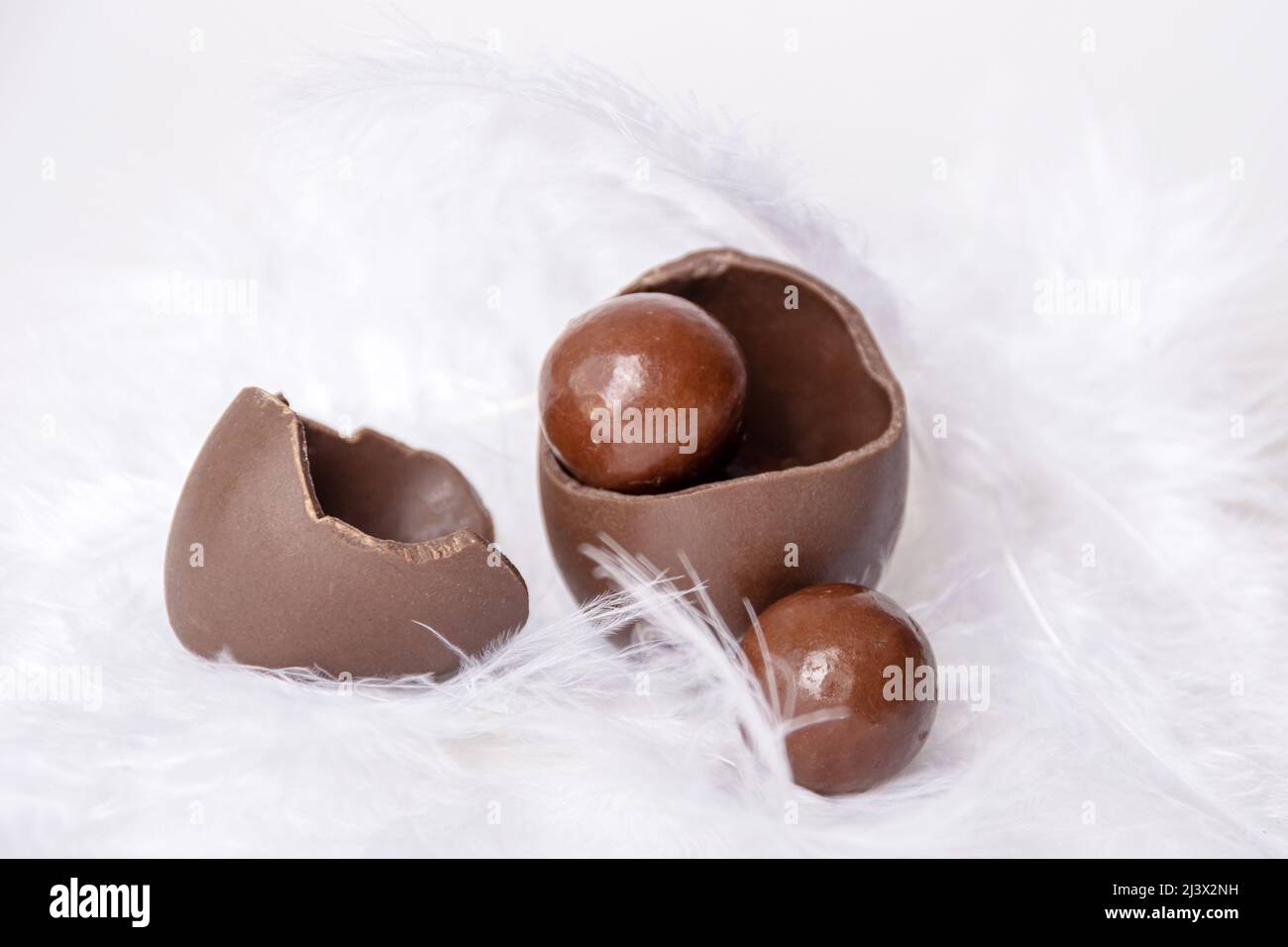 Œuf de pâques au chocolat fissuré avec de petits bonbons ronds au chocolat et une coquille d'œuf vide dans un nid de plumes blanches, espace de copie. Chocolat pour les enfants. E Banque D'Images