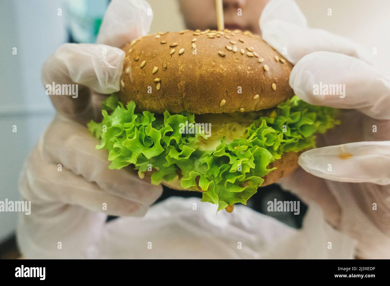 Homme en gants de caoutchouc tenant un hamburger. Banque D'Images