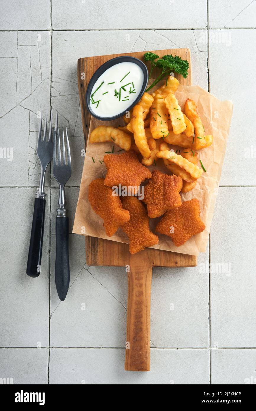 Fish Chips, restauration rapide britannique. Les bâtonnets de poisson aux frites sont fixés sur un panneau rustique, sur un fond de table de comptoir en carreaux gris craquelés. Tradition Banque D'Images