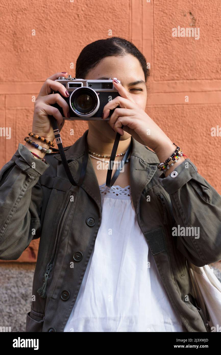 Portrait d'une jeune femme de race mixte prenant des photos avec son appareil photo. Elle est à l'extérieur et porte des vêtements décontractés. Banque D'Images