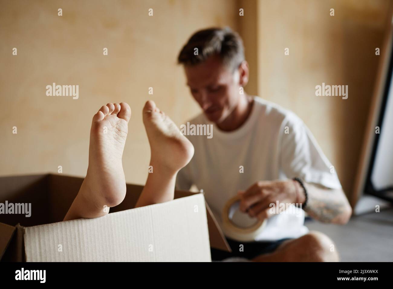 Gros plan des pieds de bébé mignons sortant de la boîte en carton pendant que la famille déplace la maison en arrière-plan, espace de copie Banque D'Images