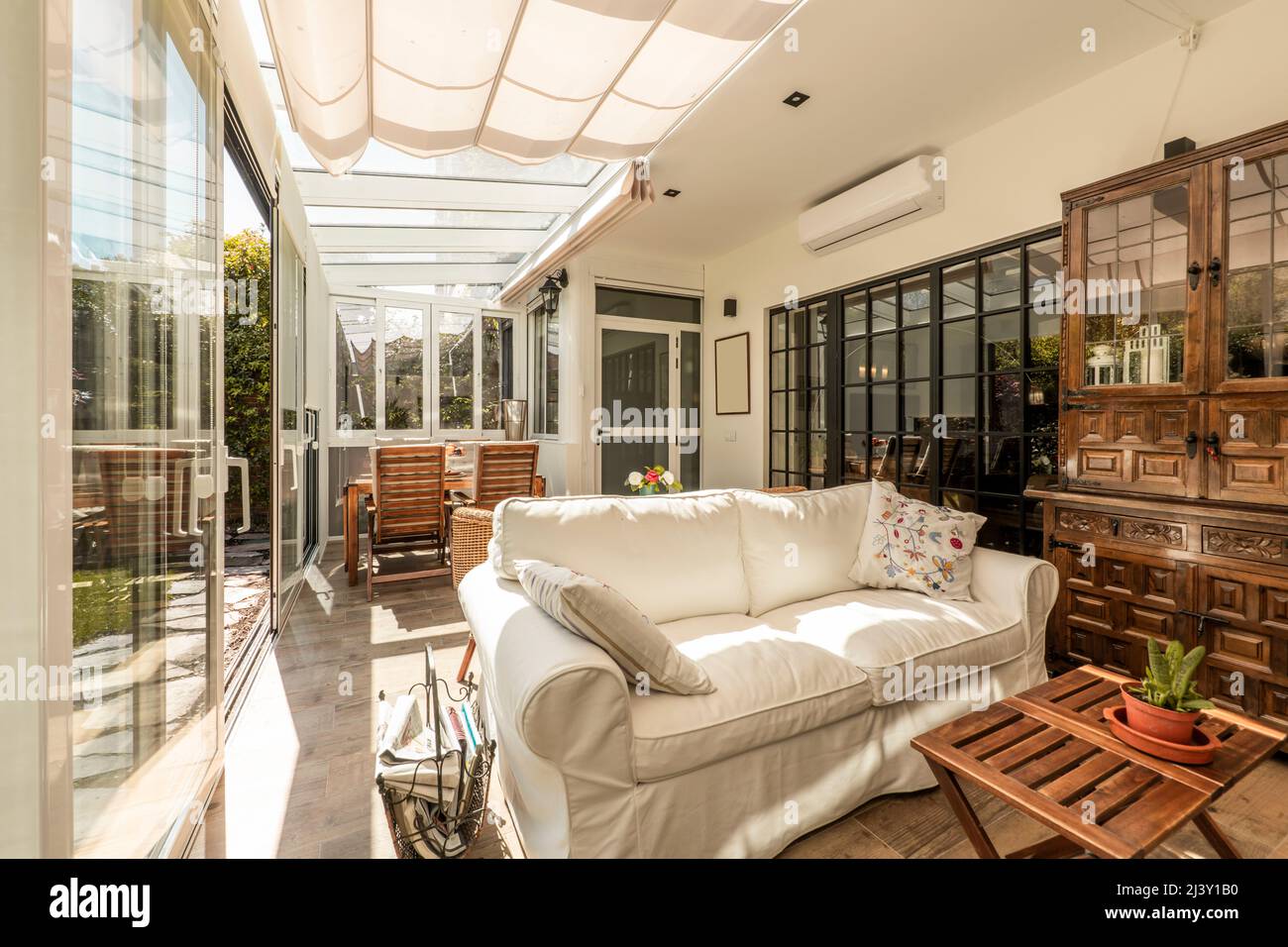 Intérieur d'une terrasse fermée en aluminium blanc et verre avec de grandes portes coulissantes avec accès à un jardin avec pelouse et plantes ornementales, salle à manger en bois Banque D'Images