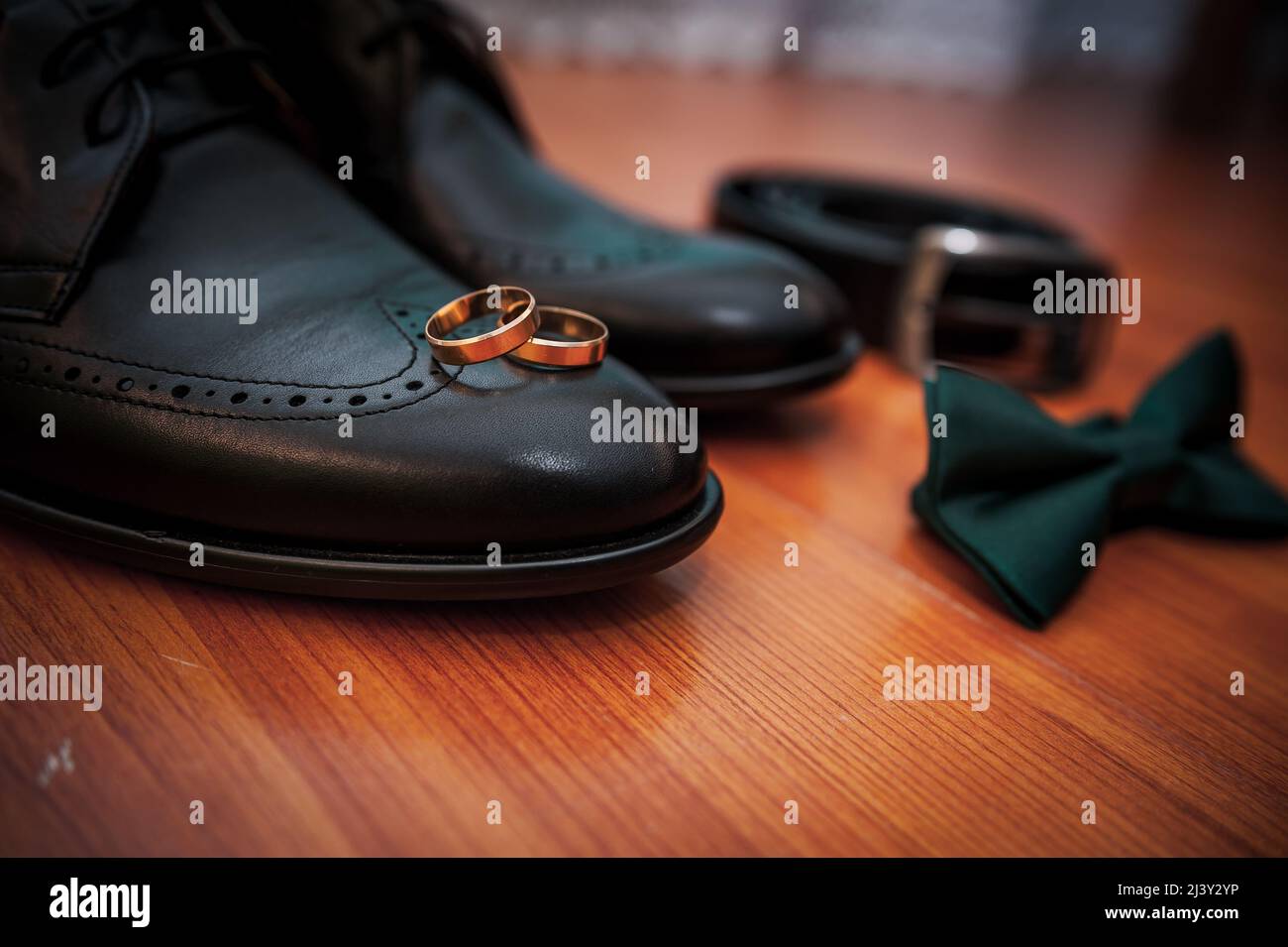 Chaussures noires en cuir, une ceinture, une paire d'anneaux dorés, une cravate papillon verte sur un fond Banque D'Images