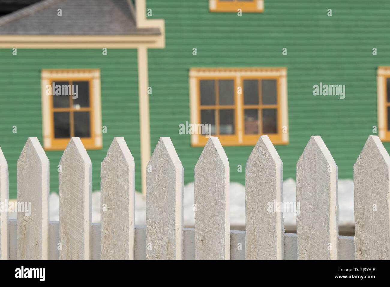 L'extérieur d'un panneau en bois de cape vert de style panneau de cape avec deux fenêtres à bordure crème brillante. Il y a de la neige au sol Banque D'Images