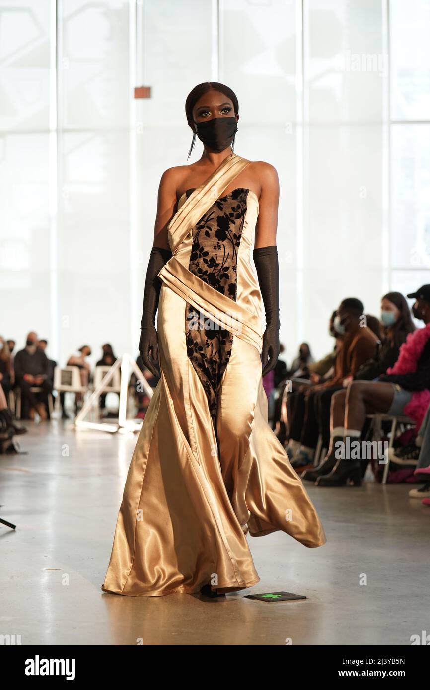 une étudiante noire portant une longue robe d'or se promenant sur la piste lors d'un événement de mode de course d'étudiant d'amatuer Banque D'Images