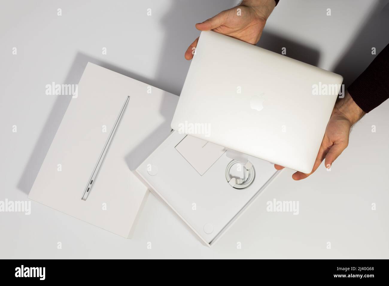 Saratov, Russie - 26 février 2022 : tenir en mains MacBook Air 13 pouces avec processeur M1, emballage avec accessoires de chargement, fond blanc Banque D'Images