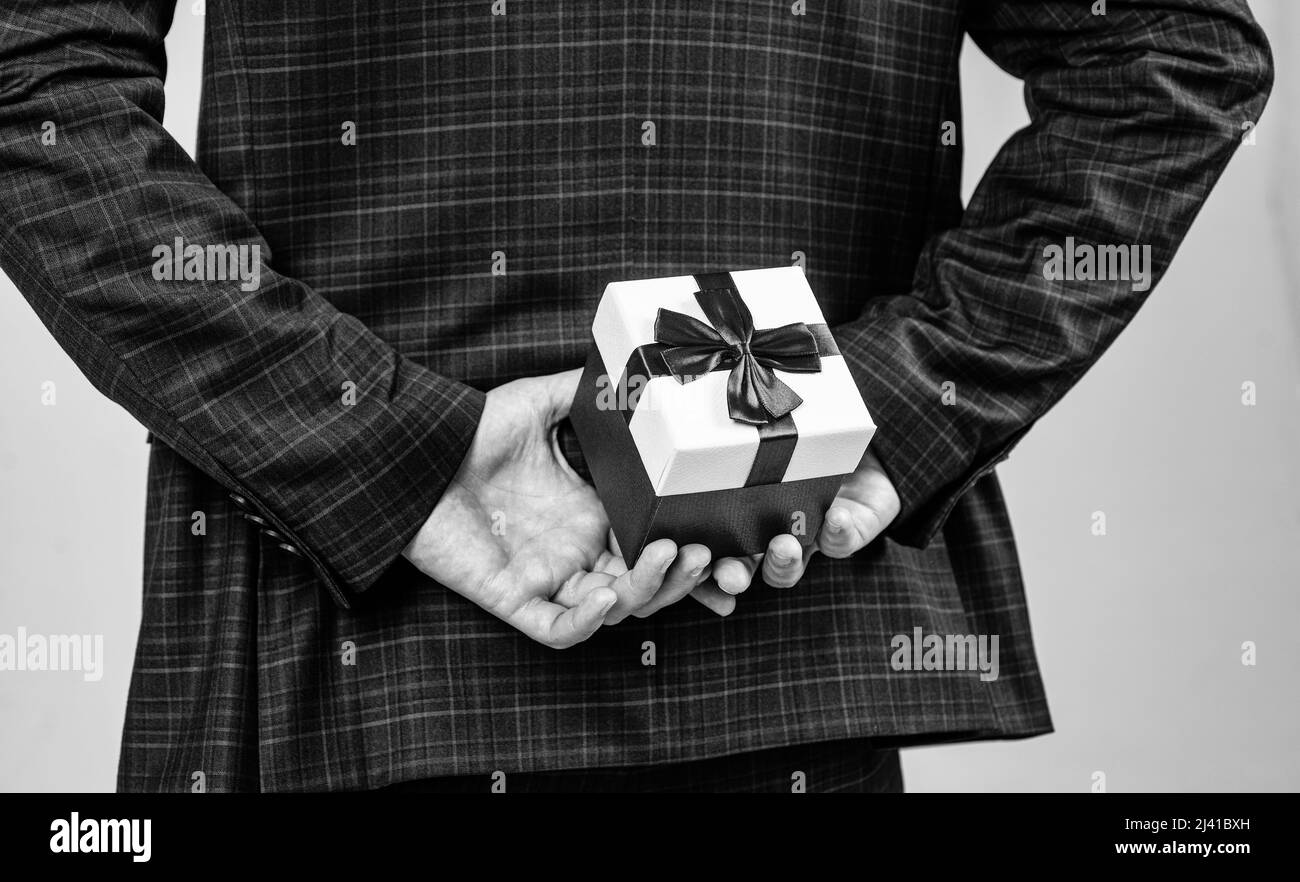Boîte de présentation avec noeud en ruban rouge tenu dans les mains des hommes derrière le dos dans un costume de mode de style formel, le lendemain de Noël Banque D'Images