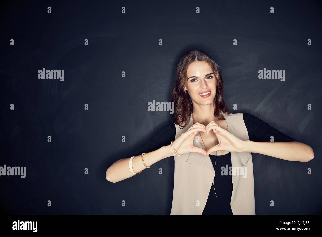 Aimer plus, haïr moins. Photo en studio d'une jeune femme attirante formant un coeur avec ses mains. Banque D'Images
