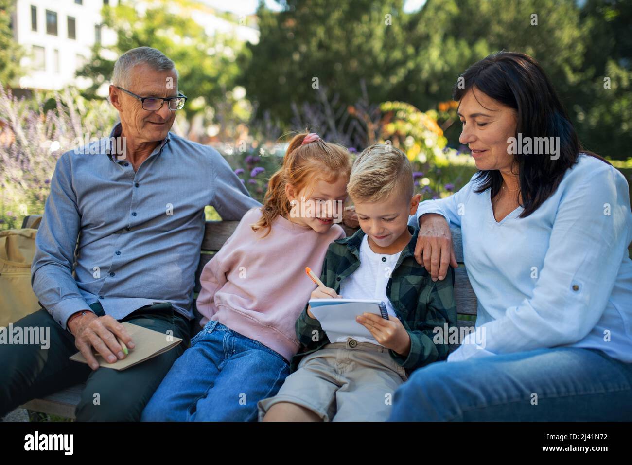 Couple senior avec petits-enfants assis sur banc et faisant de la maison dehors dans le parc. Banque D'Images