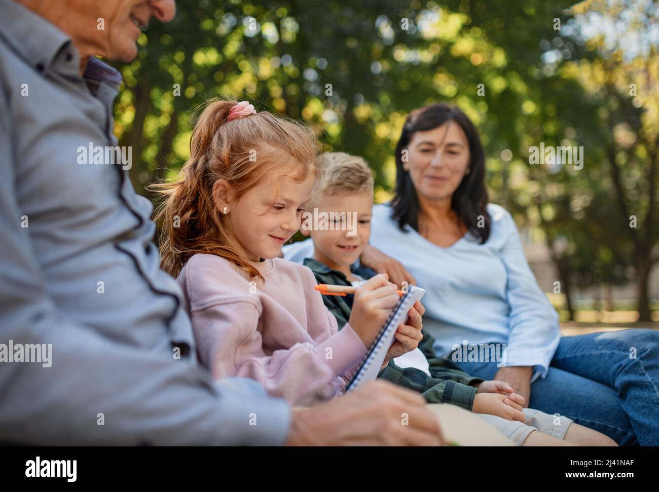 Couple senior avec petits-enfants assis sur banc et faisant de la maison dehors dans le parc. Banque D'Images