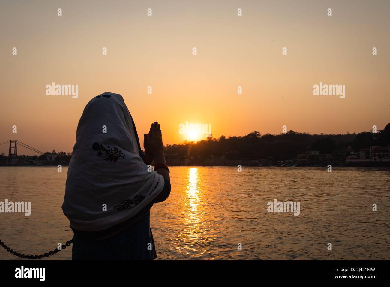 une jeune fille indienne priant le fleuve saint gange et le soleil se coucher à l'horizon à l'image de la rive du fleuve ganga est prise à la rive du fleuve rishikesh uttrakhand inde Banque D'Images