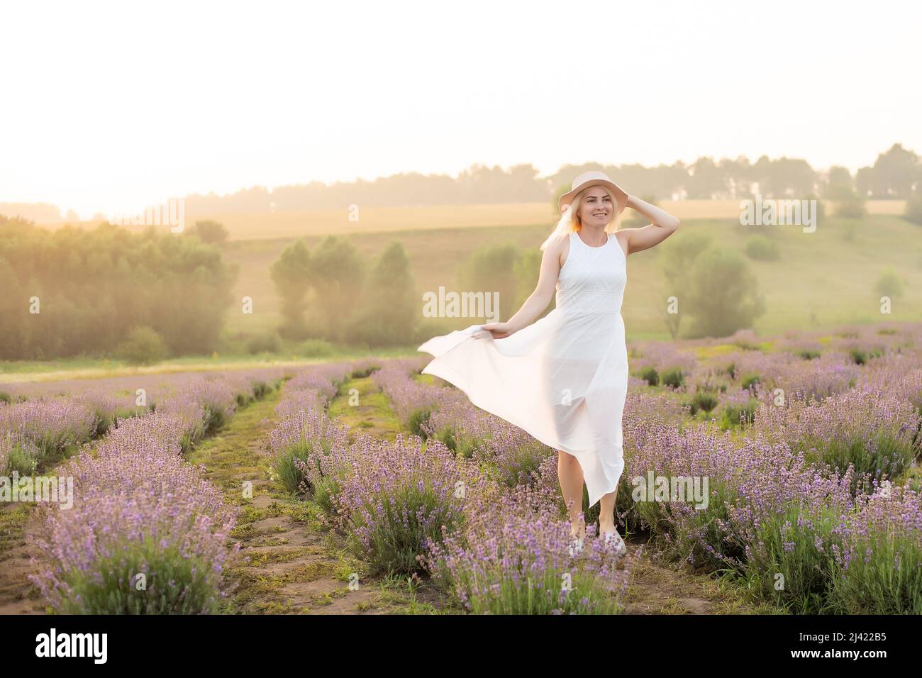 Belle jeune femme marchant dans le champ de la lavande. Robe de costume mode, chapeau de paille. Banque D'Images