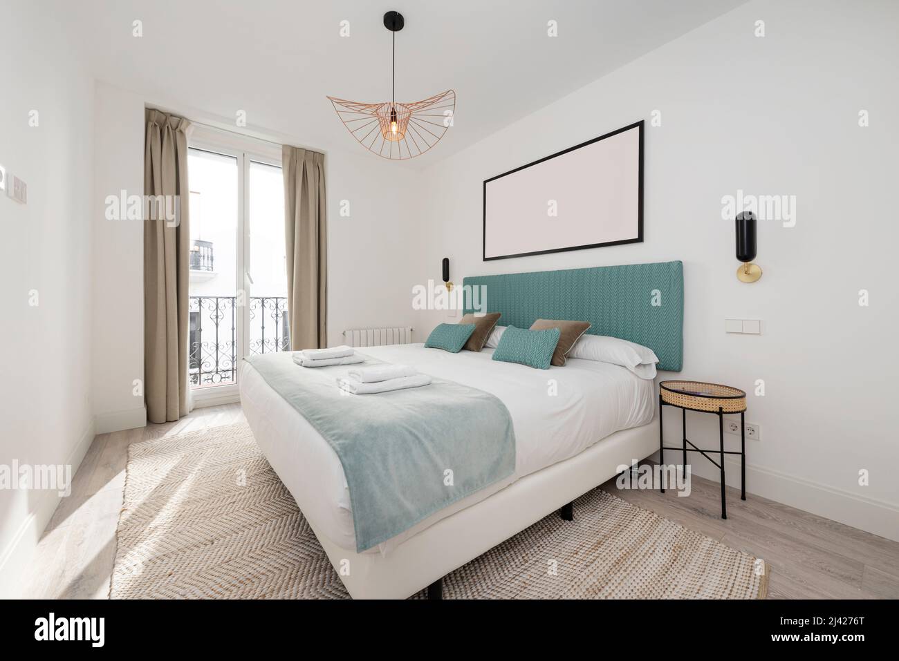 Chambre avec grand lit double, tête de lit rembourrée en tissu bleu clair, couverture en velours assortie, tapis en denim assorti et balcon avec rideaux Banque D'Images