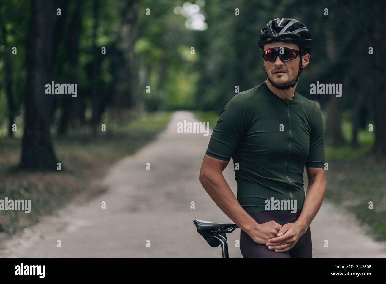 Portrait d'un athlète de sexe masculin portant un casque de sécurité et des lunettes à miroir posé à l'extérieur avec un vélo noir. Vélo le matin au parc vert. Copier la flèche Banque D'Images