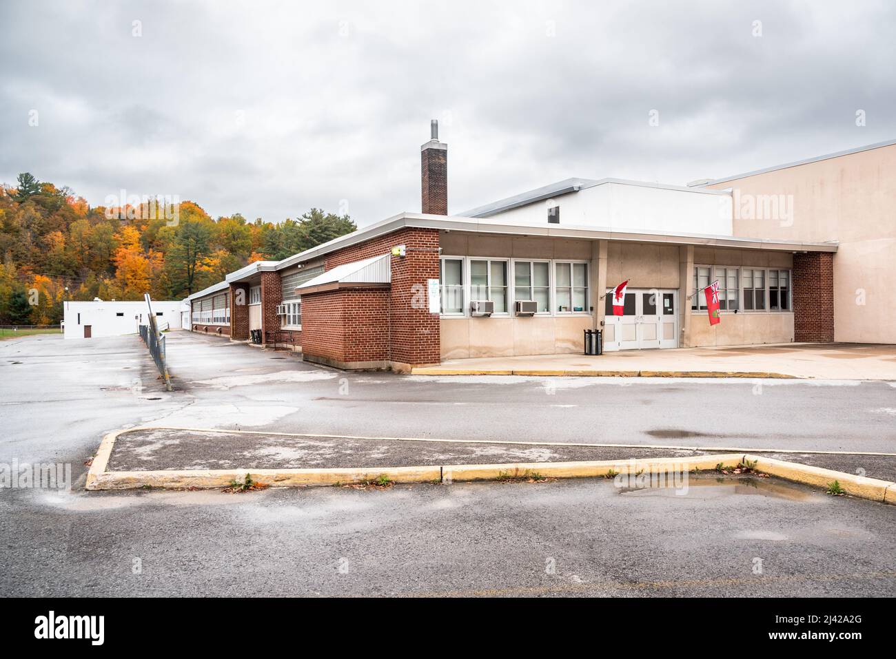 Extérieur d'un bâtiment scolaire par une journée d'automne nuageux. Les arbres d'automne colorés sont en arrière-plan. Banque D'Images
