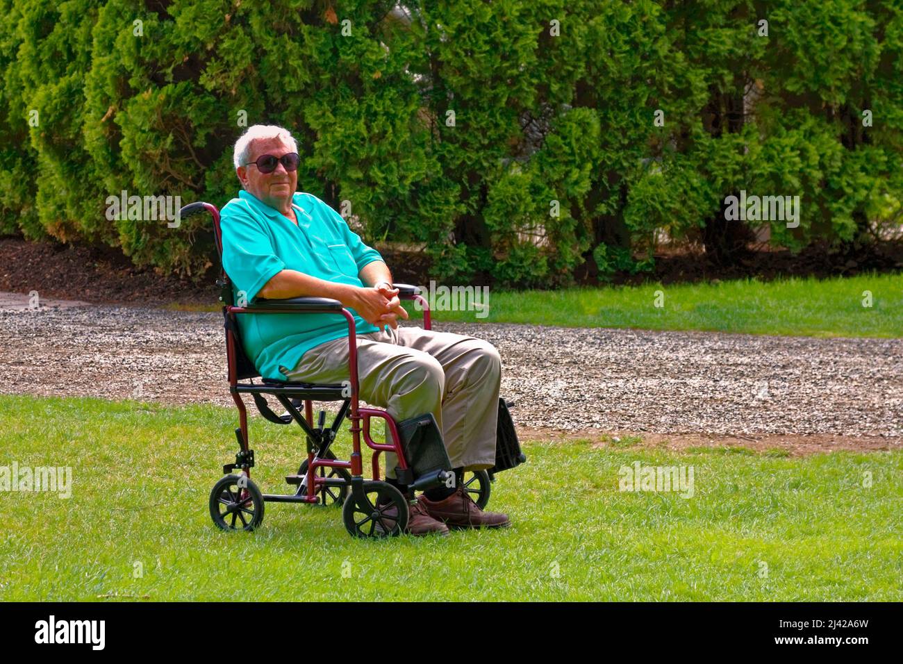 homme âgé; chaise de transport; cheveux blancs; sourire; aide à la mobilité; en attente ; extérieur, environnement naturel, herbe verte, arbres, Horizontal ; MR Banque D'Images