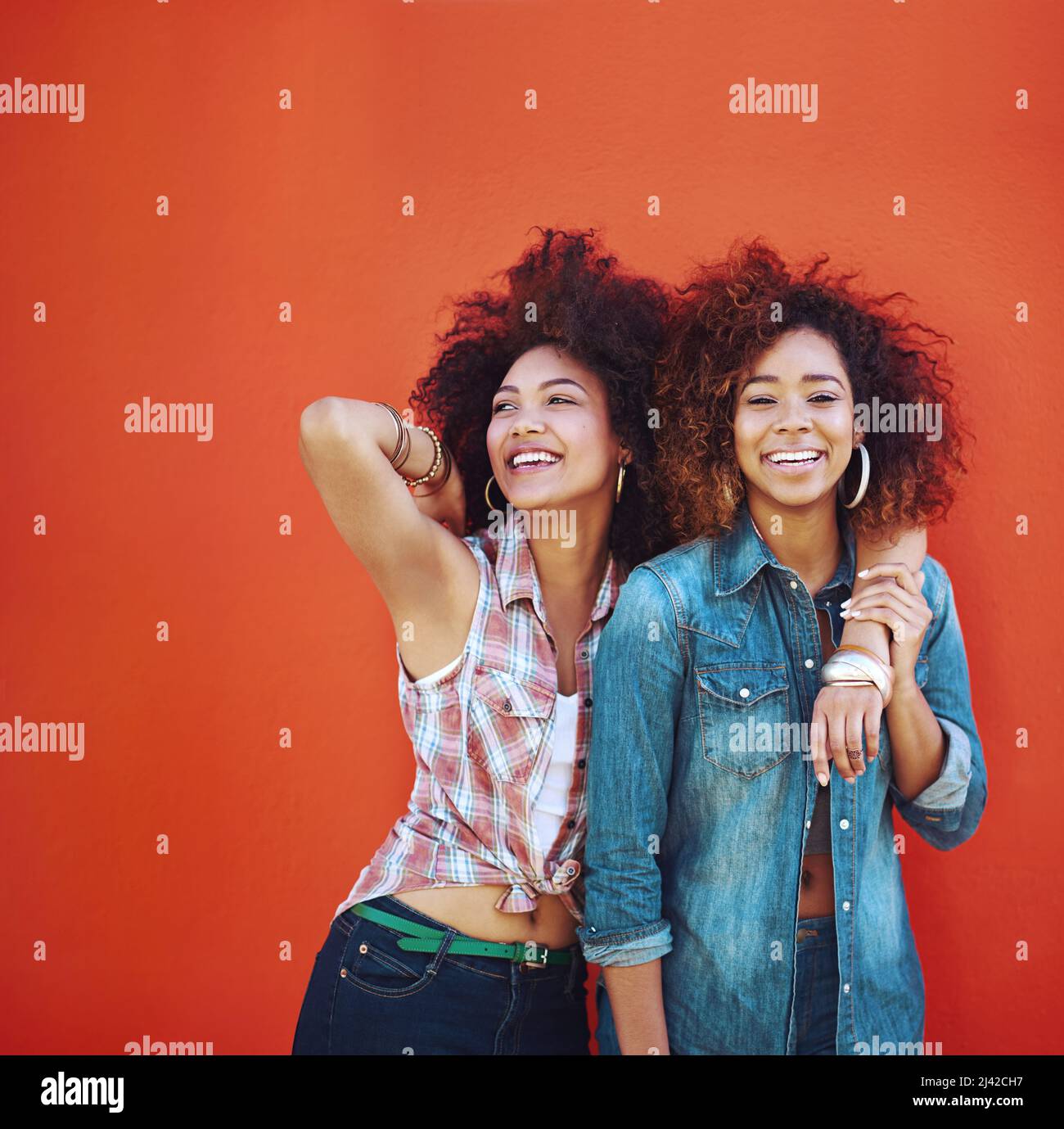 Les meilleurs amis rendent les moments heureux encore plus heureux. Photo de deux jeunes amis se posant sur un fond rouge. Banque D'Images